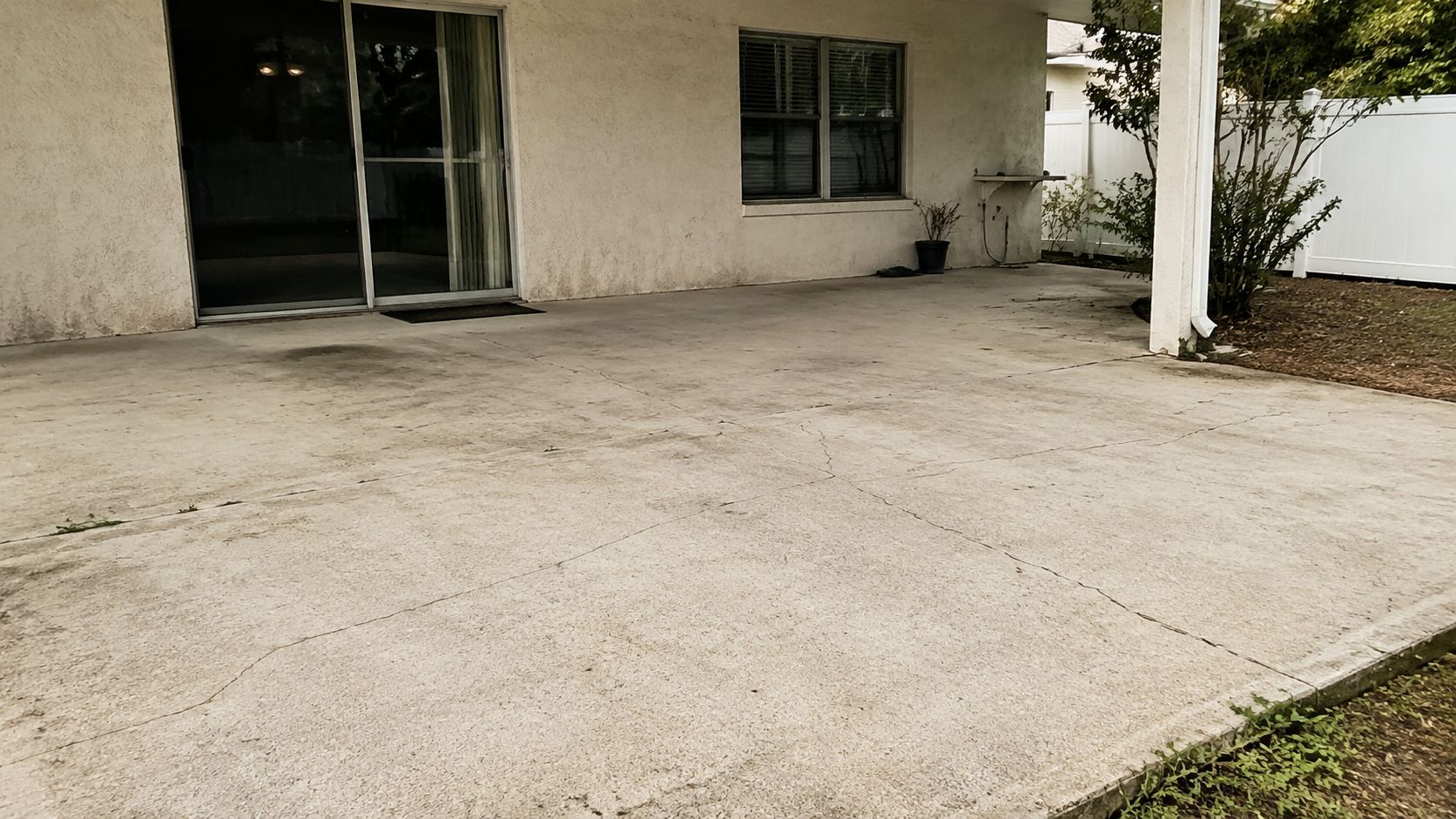 A worn concrete patio surface showing cracks near a sliding glass door and a home exterior wall.