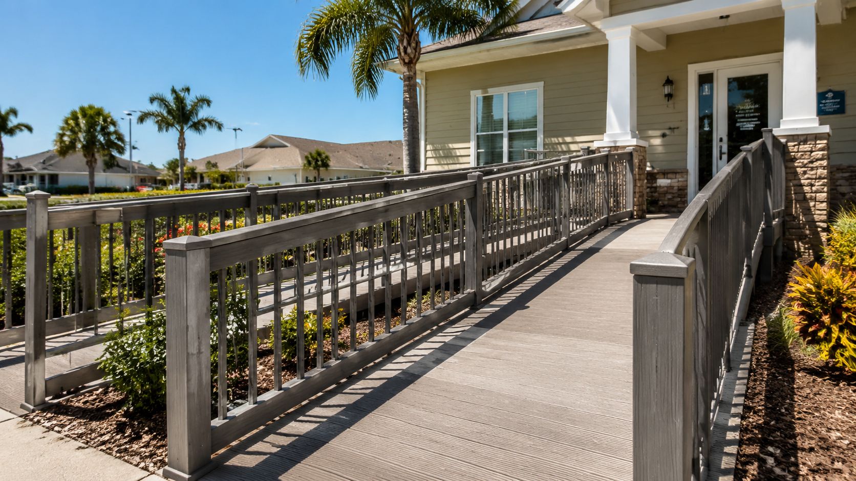 A wooden accessibility ramp with gray railings leading to the entrance of a building on a sunny day.
