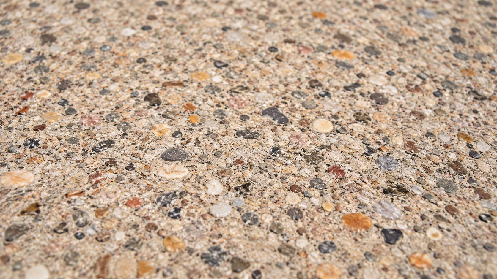 A close up texture of exposed aggregate concrete showing various small multicolored pebbles embedded in cement.